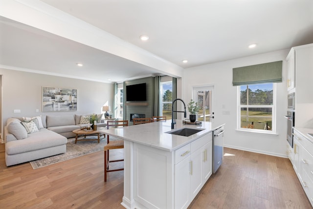 kitchen featuring appliances with stainless steel finishes, white cabinetry, sink, a center island with sink, and light hardwood / wood-style flooring