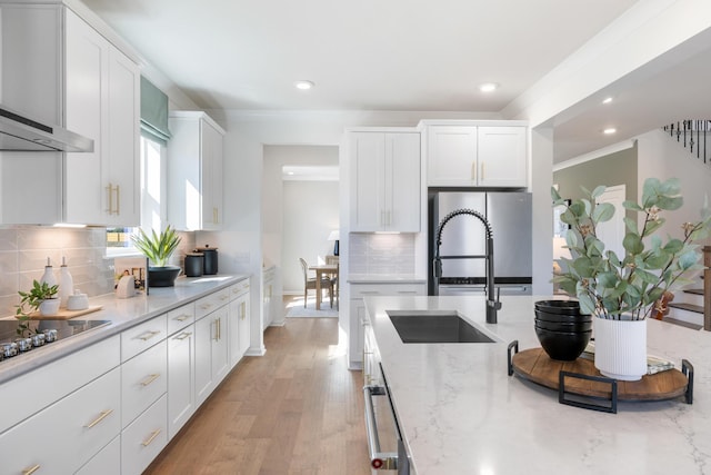 kitchen featuring sink, stainless steel fridge, white cabinets, light stone counters, and wall chimney exhaust hood