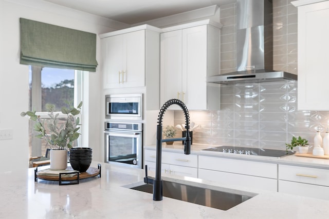 kitchen with wall chimney exhaust hood, tasteful backsplash, white cabinetry, appliances with stainless steel finishes, and light stone countertops