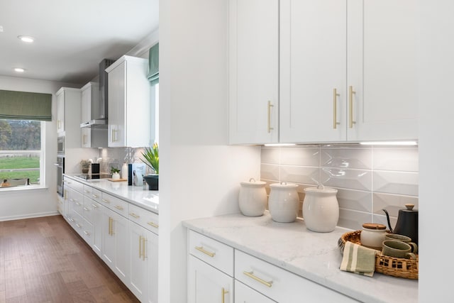 kitchen featuring white cabinetry, decorative backsplash, light stone countertops, dark wood-type flooring, and wall chimney exhaust hood