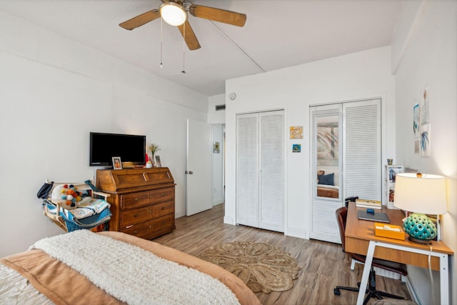 bedroom with two closets, wood-type flooring, and ceiling fan