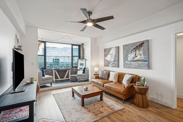 living room with a wall of windows, ceiling fan, and light wood-type flooring