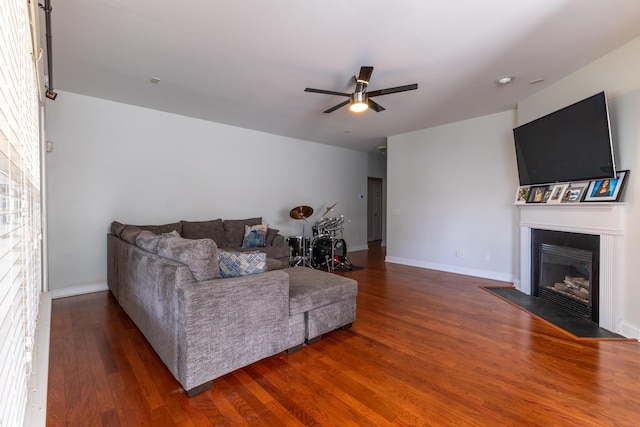 living room with baseboards, a fireplace with flush hearth, a ceiling fan, and wood finished floors