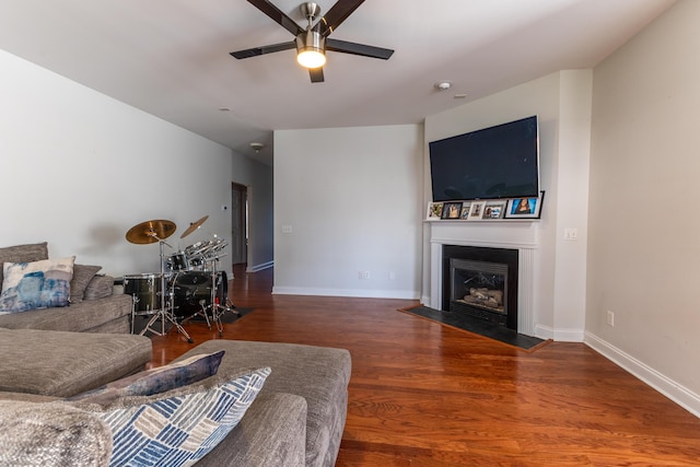 living area featuring a fireplace with flush hearth, a ceiling fan, baseboards, and wood finished floors