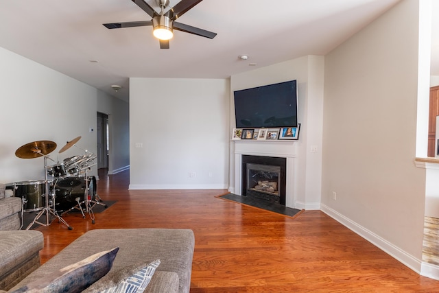 living area featuring a fireplace with flush hearth, a ceiling fan, baseboards, and wood finished floors