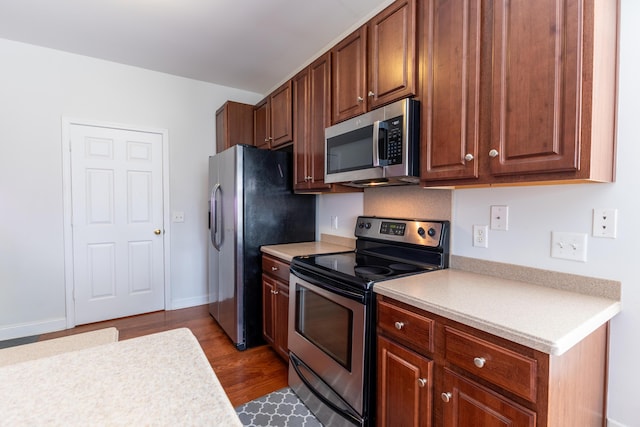 kitchen with stainless steel appliances, light countertops, baseboards, and wood finished floors