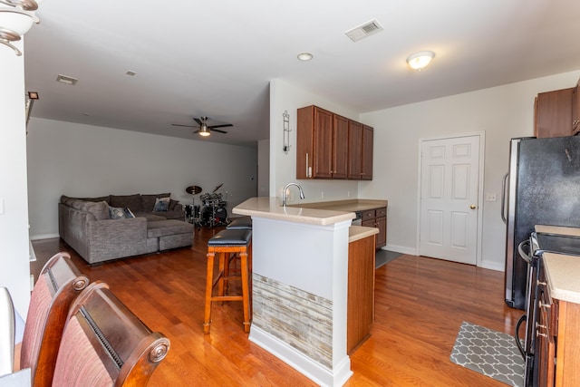 kitchen featuring a breakfast bar area, light countertops, wood finished floors, range with electric cooktop, and a peninsula