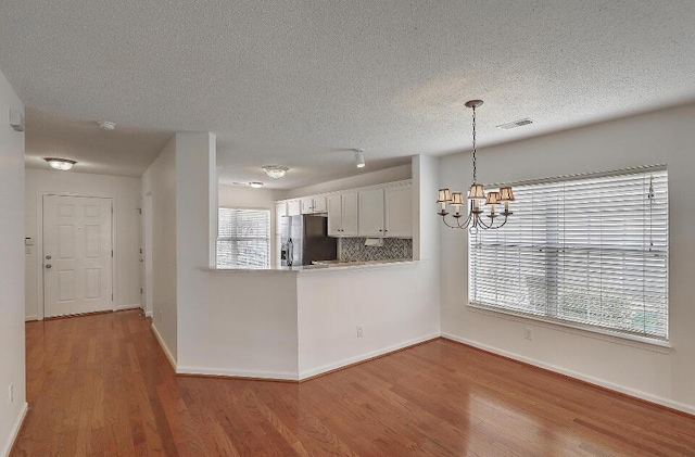 159 Townsend Way, Summerville, SC 29483 - kitchen with black fridge with ice dispenser, a chandelier, wood finished floors, a textured ceiling, and white cabinets