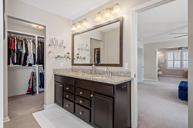 full bathroom with double vanity, a spacious closet, a sink, ceiling fan, and baseboards