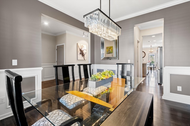 dining room featuring a decorative wall, a wainscoted wall, wood finished floors, an inviting chandelier, and crown molding