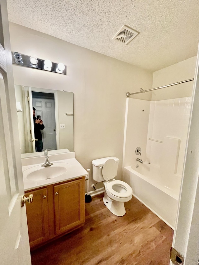 full bathroom featuring visible vents, toilet, a textured ceiling, wood finished floors, and vanity