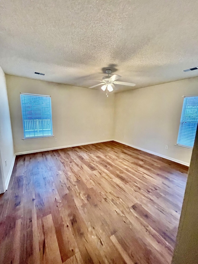 unfurnished room featuring ceiling fan, visible vents, baseboards, and wood finished floors