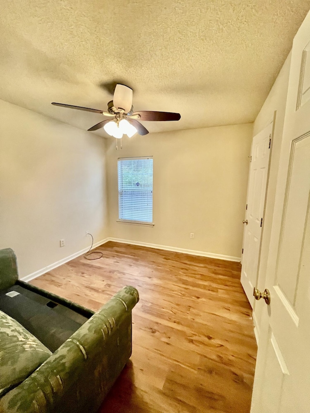 living area with baseboards, a textured ceiling, wood finished floors, and a ceiling fan