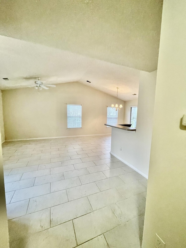 spare room featuring lofted ceiling, ceiling fan with notable chandelier, baseboards, and a textured ceiling