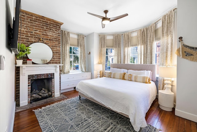 bedroom with ceiling fan, hardwood / wood-style floors, a brick fireplace, and baseboards