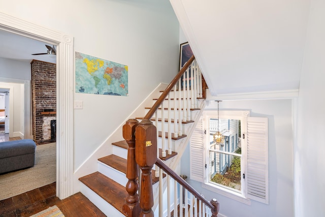 staircase with a fireplace, wood finished floors, a ceiling fan, and baseboards