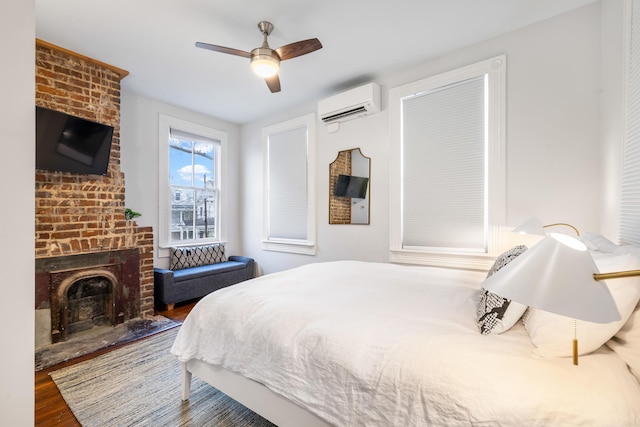 bedroom featuring a brick fireplace, a wall mounted air conditioner, ceiling fan, and wood finished floors