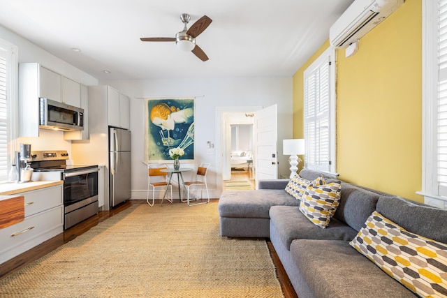 living area with a ceiling fan, baseboards, light wood finished floors, and a wall mounted AC