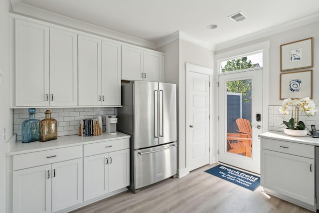 kitchen featuring visible vents, ornamental molding, freestanding refrigerator, light wood-style floors, and backsplash