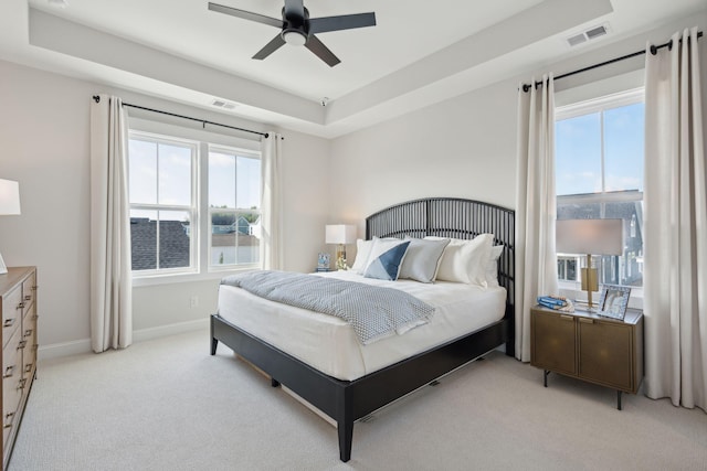 bedroom with light carpet, multiple windows, visible vents, and a tray ceiling