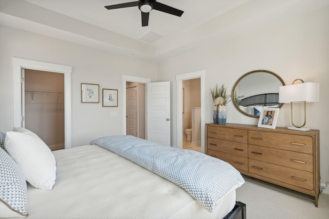 bedroom with a walk in closet, a closet, light colored carpet, a raised ceiling, and connected bathroom