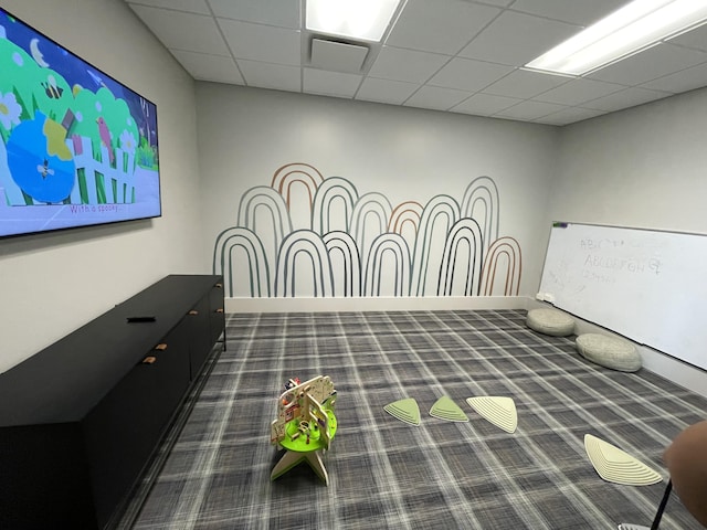 recreation room with dark colored carpet, a paneled ceiling, and baseboards