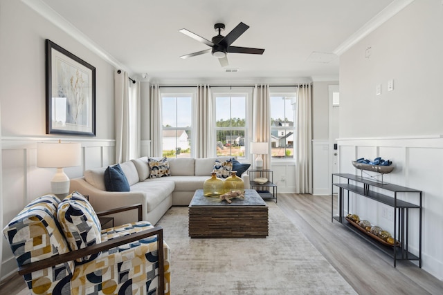 living area with light wood-type flooring, a wainscoted wall, crown molding, and ceiling fan