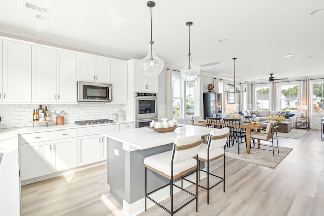 kitchen with visible vents, decorative backsplash, appliances with stainless steel finishes, open floor plan, and white cabinets