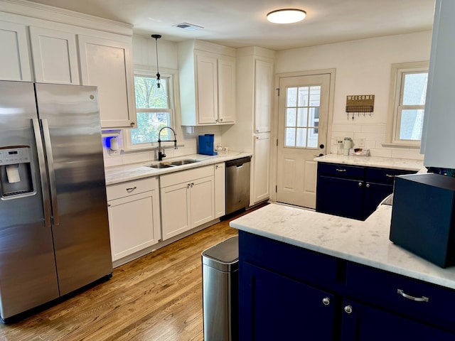 kitchen featuring stainless steel appliances, white cabinetry, a sink, and hanging light fixtures