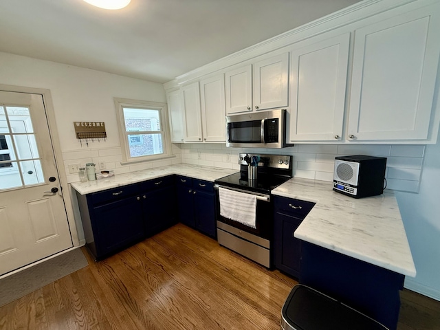 kitchen with stainless steel appliances, wood finished floors, backsplash, white cabinets, and light stone countertops