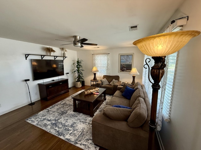 living room featuring dark wood-style floors, visible vents, baseboards, and a ceiling fan