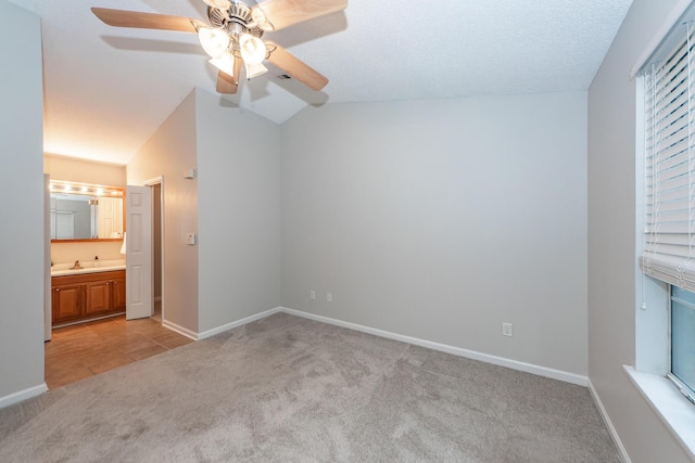 unfurnished bedroom with lofted ceiling, ensuite bathroom, ceiling fan, a textured ceiling, and light colored carpet