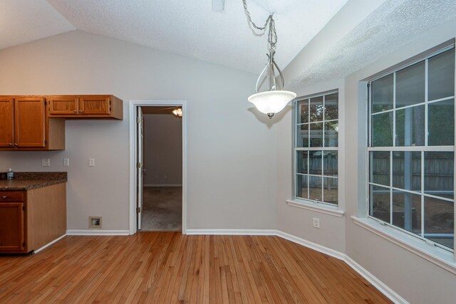 kitchen with vaulted ceiling, a textured ceiling, decorative light fixtures, and light wood-type flooring