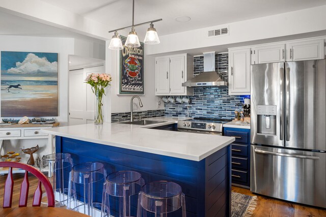 kitchen featuring backsplash, sink, decorative light fixtures, appliances with stainless steel finishes, and wall chimney exhaust hood