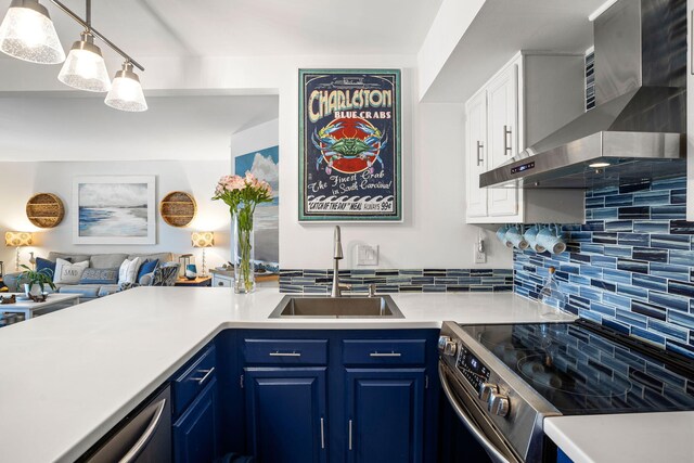 kitchen with wall chimney exhaust hood, tasteful backsplash, blue cabinets, sink, and stainless steel appliances