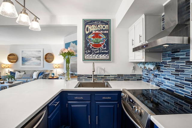 kitchen with blue cabinets, a sink, appliances with stainless steel finishes, wall chimney range hood, and decorative backsplash