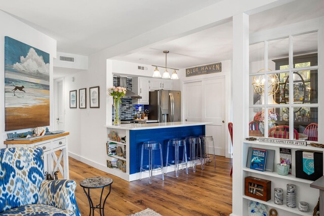 kitchen with dark hardwood / wood-style floors, hanging light fixtures, a kitchen bar, a notable chandelier, and stainless steel fridge with ice dispenser