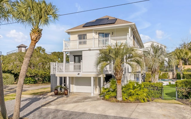 coastal home featuring solar panels, a garage, concrete driveway, fence, and a balcony