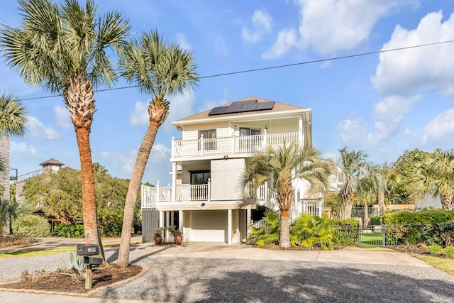 raised beach house featuring a balcony, stucco siding, driveway, solar panels, and a garage