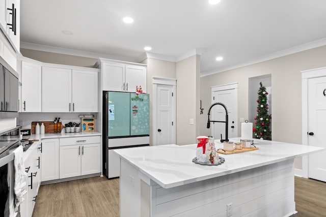 kitchen featuring light stone countertops, stainless steel oven, refrigerator, a center island with sink, and white cabinets