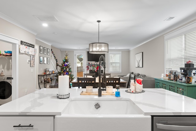 kitchen featuring stainless steel dishwasher, decorative light fixtures, washer / dryer, and a center island with sink