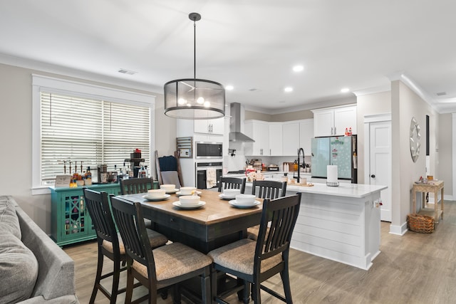 dining area with light hardwood / wood-style floors, crown molding, and sink