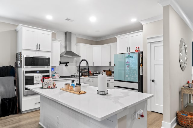 kitchen with white cabinetry, a center island with sink, wall chimney exhaust hood, and appliances with stainless steel finishes