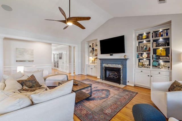 living area with built in features, light wood-style floors, a fireplace with flush hearth, vaulted ceiling, and ceiling fan