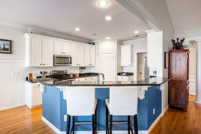 kitchen with white cabinets, light wood finished floors, a breakfast bar area, and stainless steel appliances