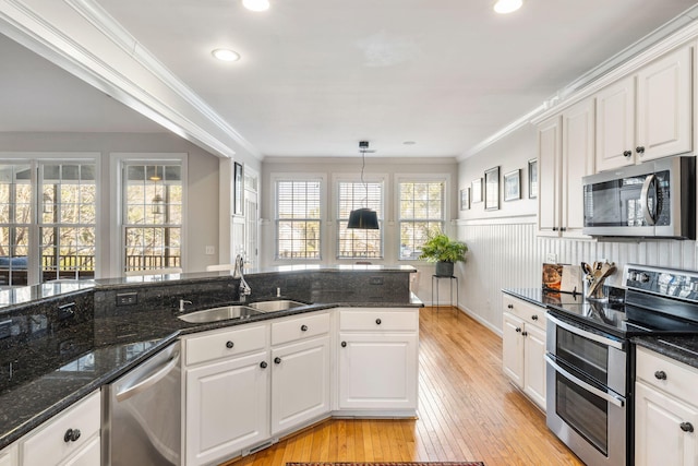 kitchen with white cabinets, ornamental molding, stainless steel appliances, light wood-style floors, and a sink