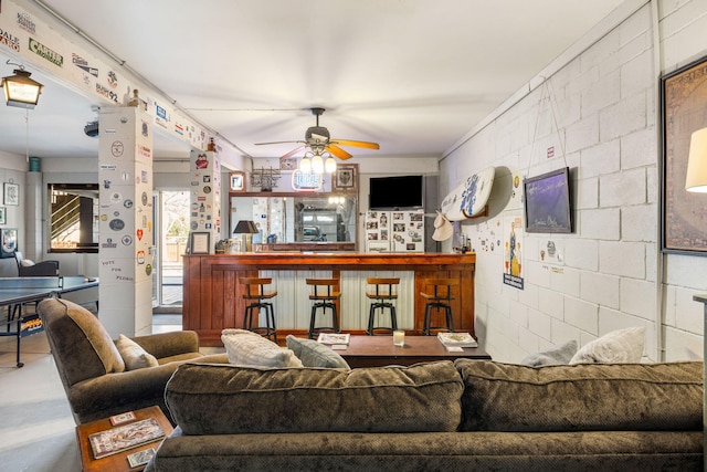 living room with a bar, a ceiling fan, and concrete block wall