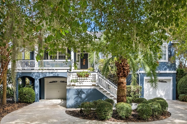 view of front of house featuring covered porch, stairway, concrete driveway, and stucco siding