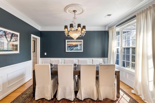 dining area with light wood-type flooring, an inviting chandelier, visible vents, and wainscoting