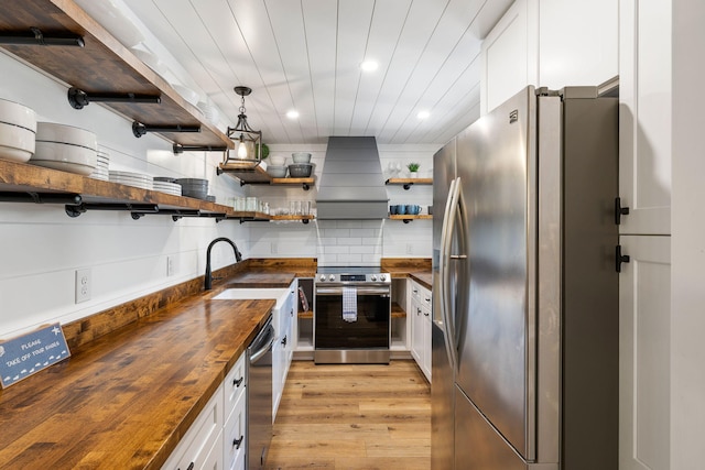 kitchen with light wood finished floors, wooden counters, open shelves, stainless steel appliances, and custom range hood